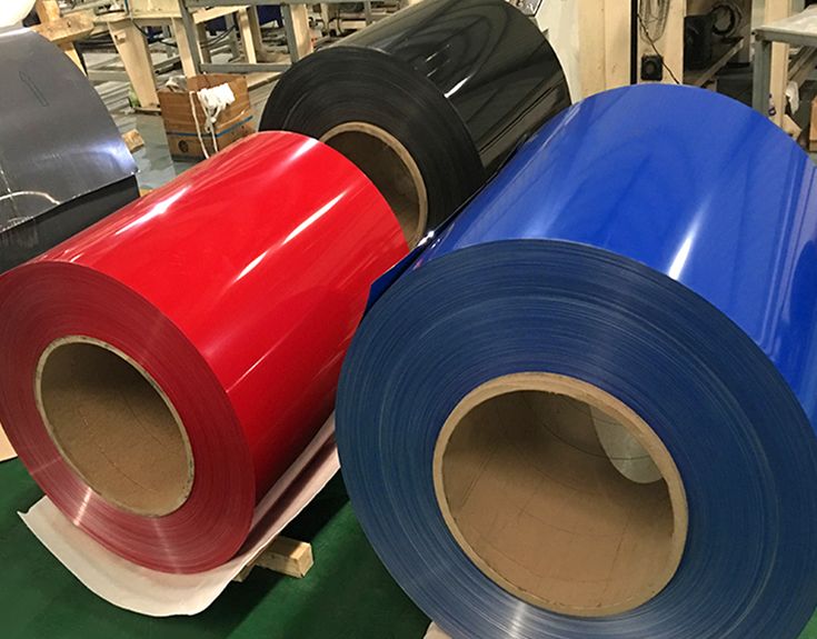 Colour-coated aluminium coils in red, blue and black, stacked and ready for roofing sheet fabrication