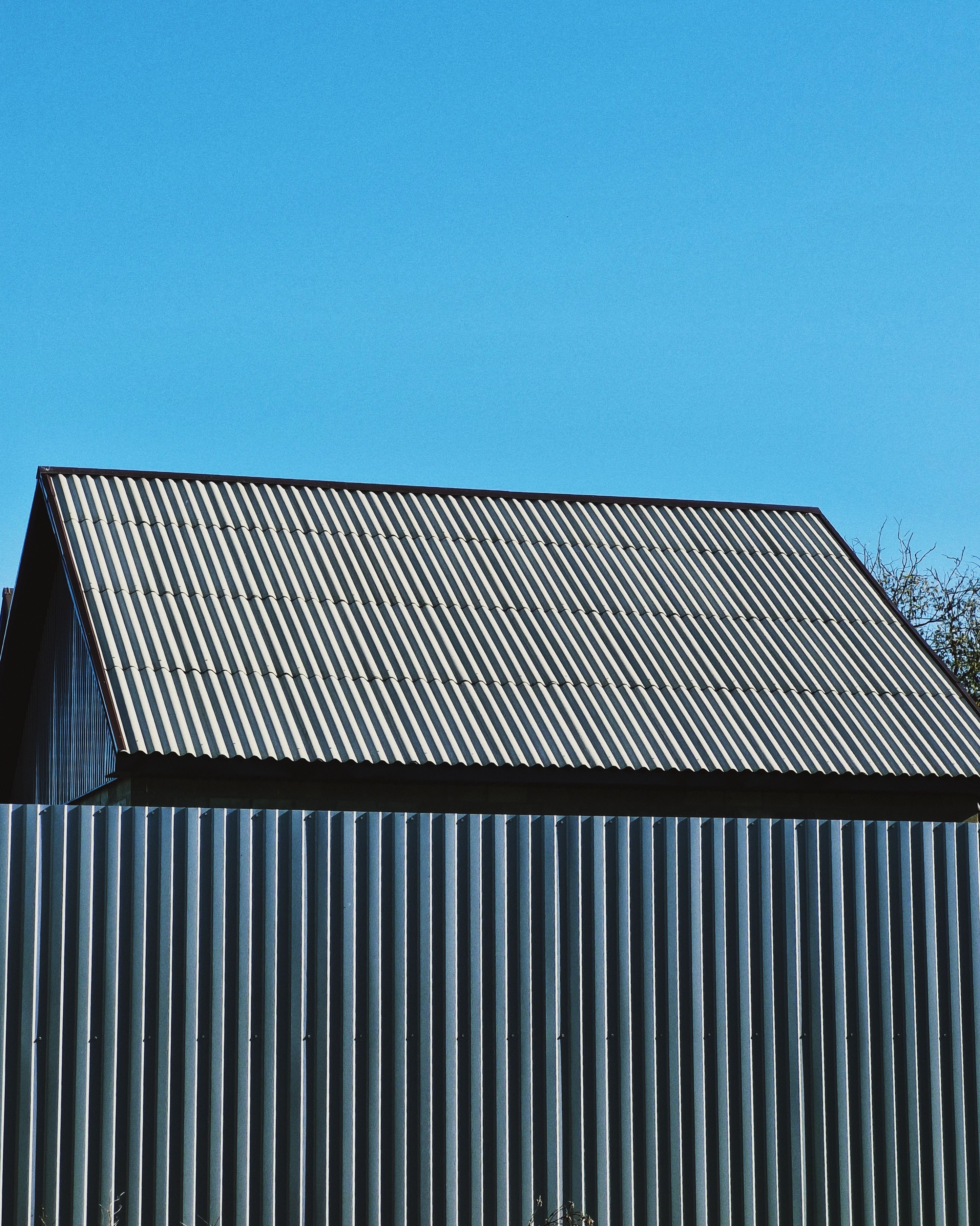 Corrugated metal roof and matching vertical wall cladding on a gable-roofed building against a clear blue sky