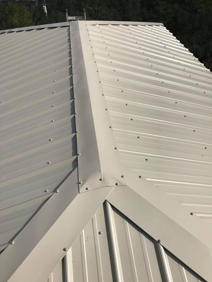 Close-up of a hip roof ridge junction on a cream-coloured corrugated metal roof, showing fastener spacing and flashing detail