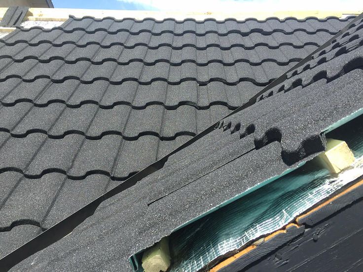 Close-up of Roman-profile stone-coated roof tiles at the ridge, showing the underlayment and valley flashing beneath